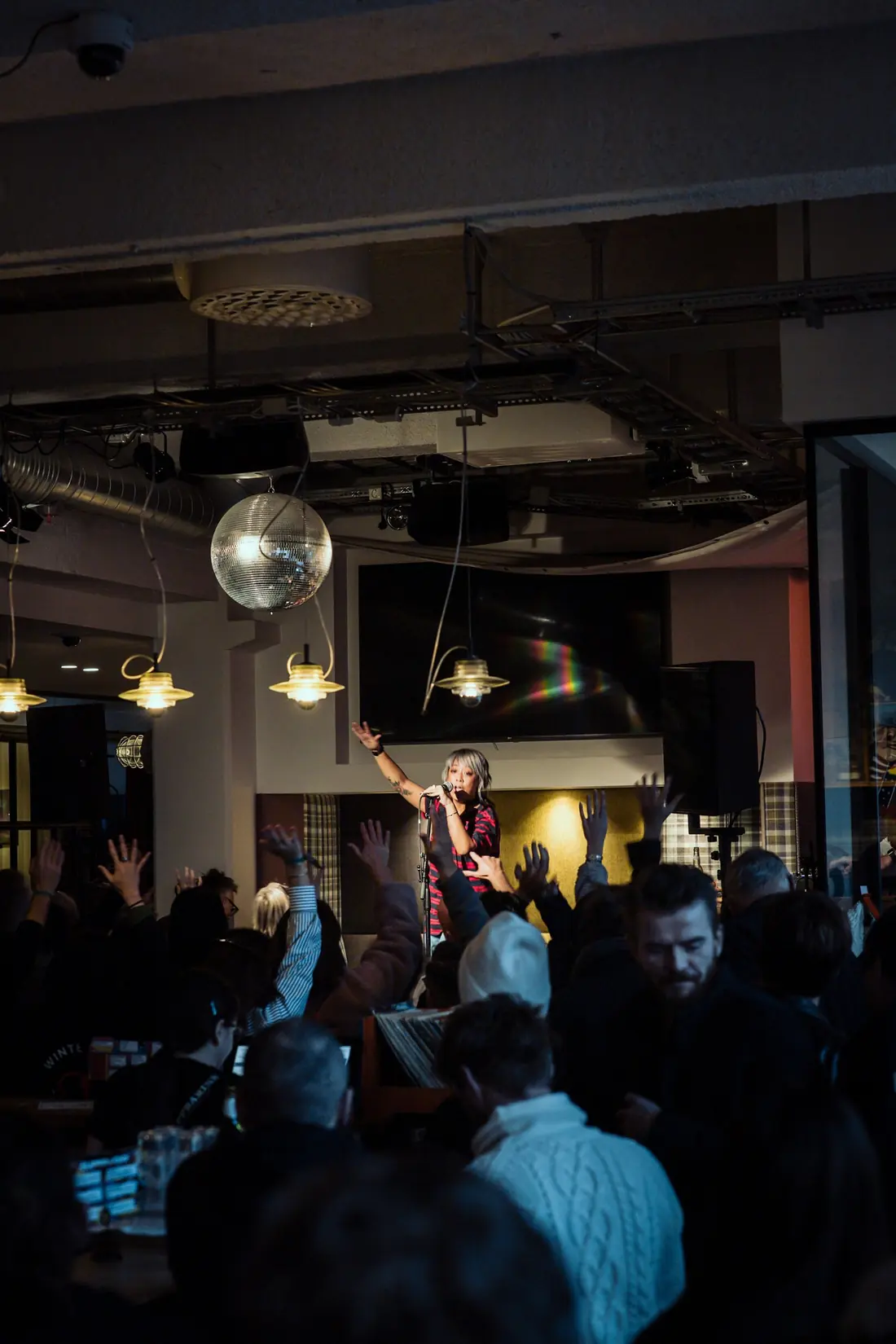 Cell7 performing in a bar while the crowd raises their hands under a disco ball