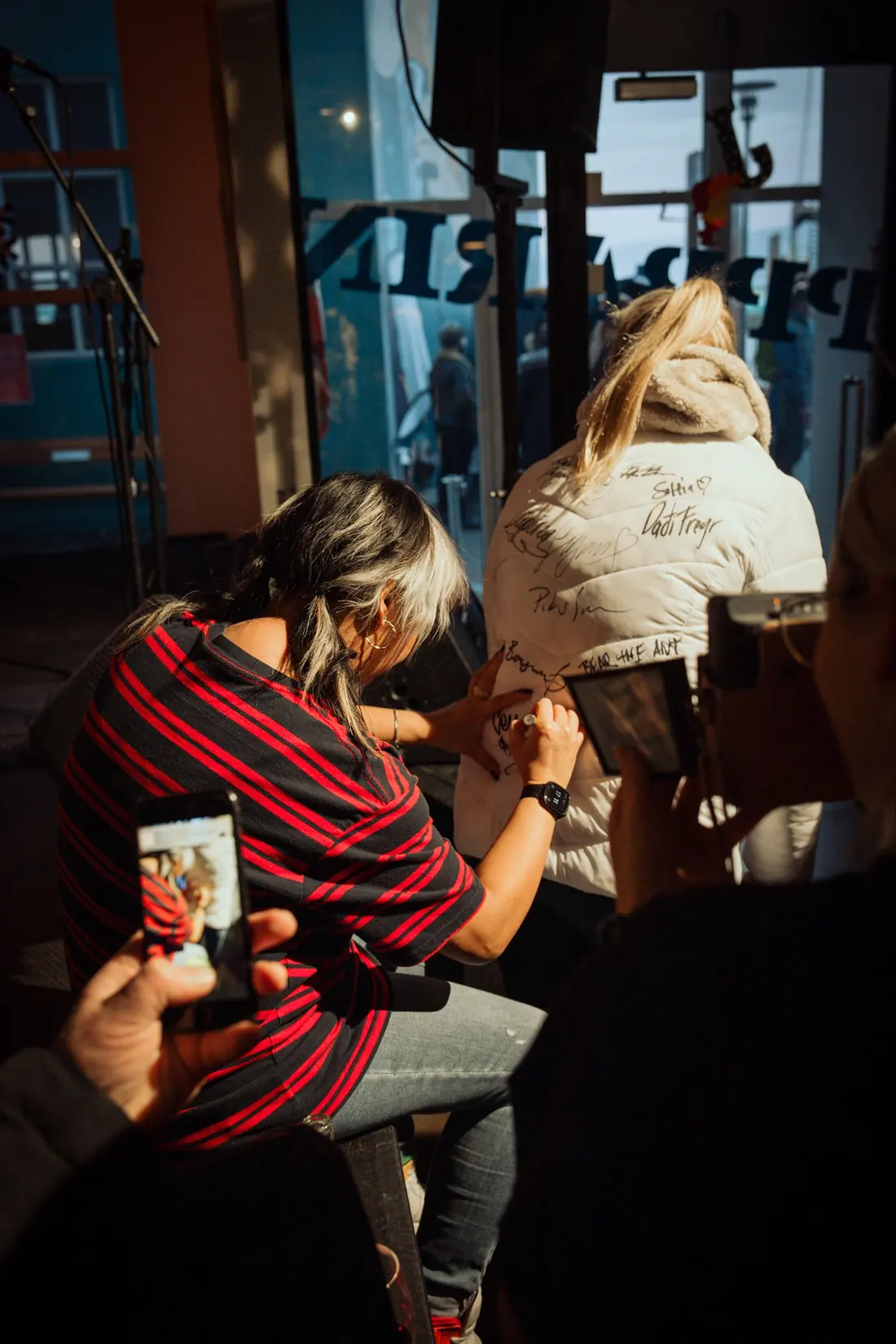 Cell7 signing a fan's white jacket while people film on their phones